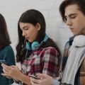 Adolescentes encostados na parede mexendo no celular.