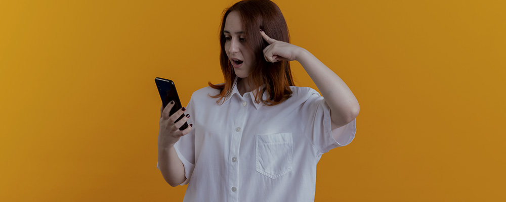 Garota surpresa colocando o dedo indicador sobre sua têmpora enquanto lê algo no celular.