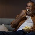 Homem assistindo os lançamentos de maio de 2024 da Netflix enquanto come pipoca.