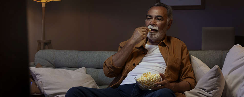 Homem assistindo os lançamentos de maio de 2024 da Netflix enquanto come pipoca.