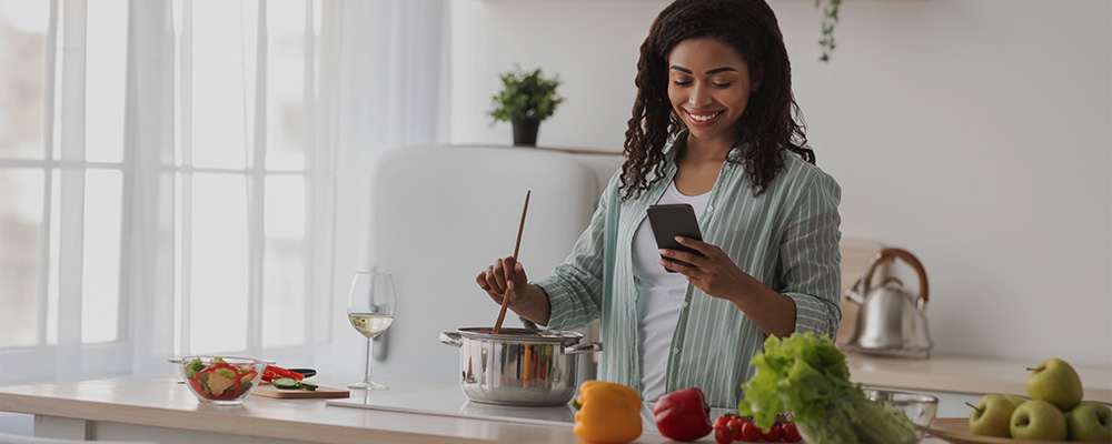 Mulher usando o celular para ajudá-la a preparar um prato.