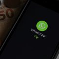 Celular com o WhatsApp Pay aberto ao lado de uma nota de cinquenta reais e várias moedas.