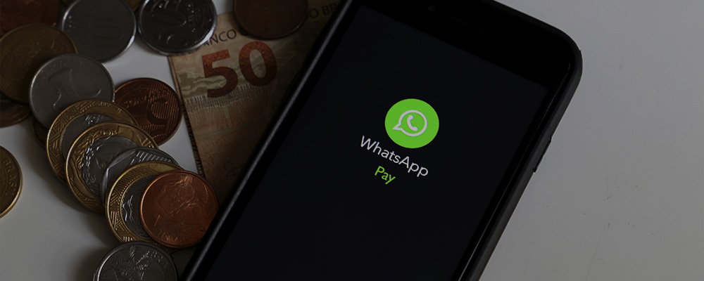 Celular com o WhatsApp Pay aberto ao lado de uma nota de cinquenta reais e várias moedas.