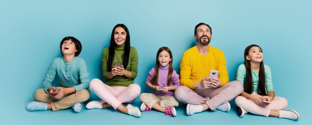 Todos os membros de uma família composta por mãe, pai e 3 filhos usando seu celulares olhando para cima.