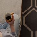 Mulher lendo no Kindle no sofá enquanto toma uma xícara de café.
