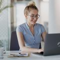 Mulher sorrindo e trabalhando com um notebook Positivo.