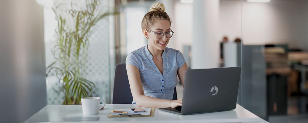 Mulher sorrindo e trabalhando com um notebook Positivo.