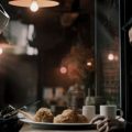 Homem e robô em uma cafeteria. O robô está mexendo no celular do homem para aumentar sua produtividade.