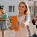 Garota fazendo sinal de positivo com o polegar na faculdade à frente de um grupo de vários alunos que têm bolsa no FIES 2024.