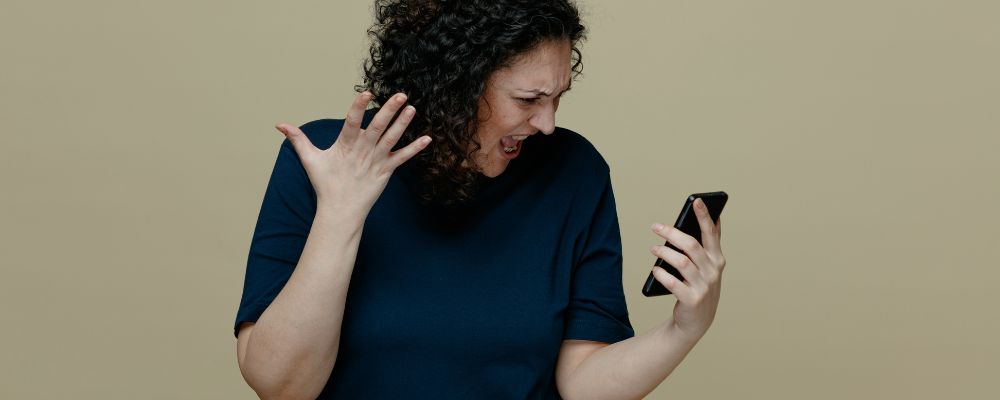 Mulher brava olhando para o celular após perceber que caiu no golpe do Pix.