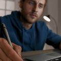 Homem assistindo aula online em um notebook e fazendo anotações em um caderno.