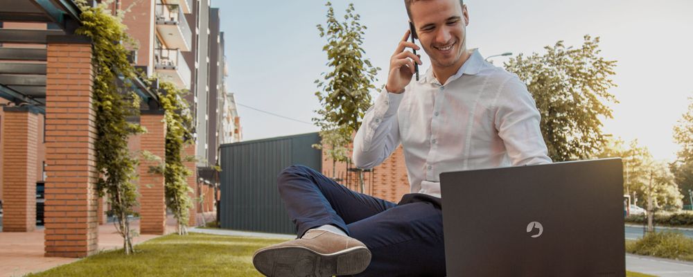 Homem falando no celular enquanto trabalha com seu notebook Positivo.