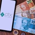 Celular com o logo do Pix ao lado de cédulas e moedas de real.