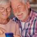 Casas de idosos usando um celular e sorrindo para a tela.