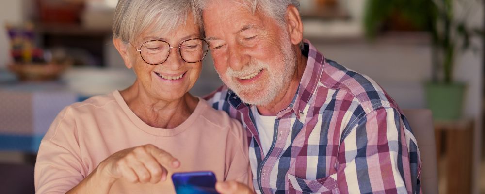 Casas de idosos usando um celular e sorrindo para a tela.