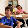 Garota ajudando um garoto com cadeira de rodas na escola, uma forma de promover acessoa à educação para crianças com deficiência.