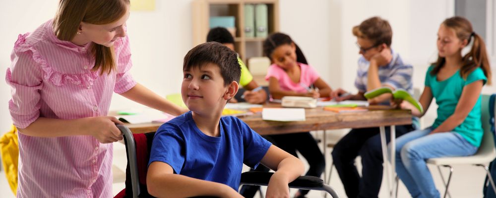 Garota ajudando um garoto com cadeira de rodas na escola, uma forma de promover acessoa à educação para crianças com deficiência.
