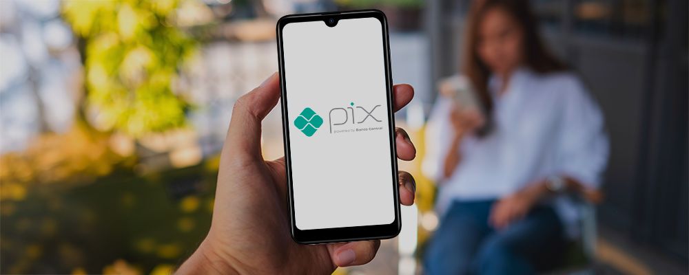 Mulher segurando um celular da Postivo com o logo do Pix aparecendo na tela.