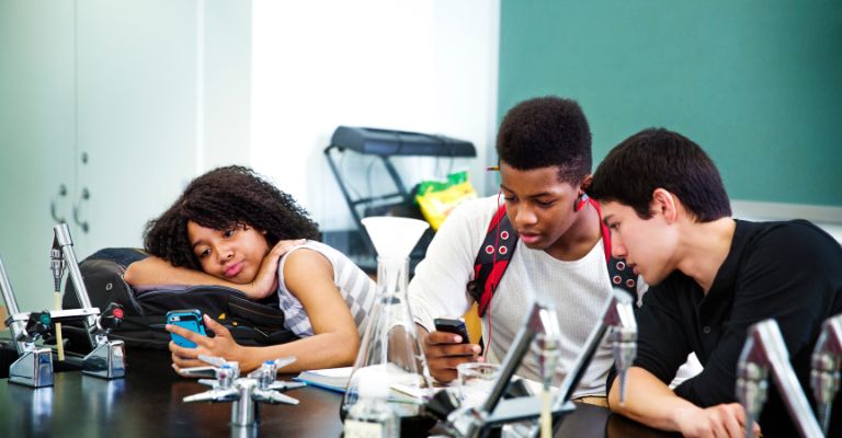 Adolescentes usando o celular para procrastinar na aula.