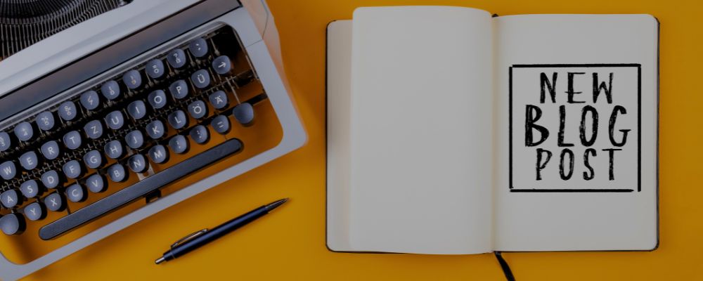 Máquina de escrever ao lado de um caderno com a frase "novo post de blog" em inglês, representando o WordPress.