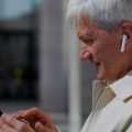 Idoso usando um celular e fones de ouvido bluetooth.