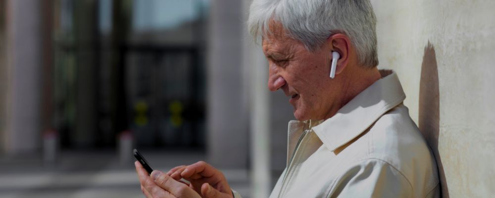 Idoso usando um celular e fones de ouvido bluetooth.