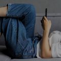 Mulher deitada no sofá controlando sua casa por meio de assistentes virtuais.