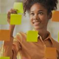 Mulher organizando as tarefas em post-its na parede, fazendo alusão ao Notion.