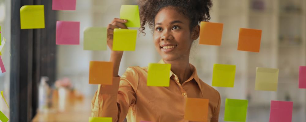 Mulher organizando as tarefas em post-its na parede, fazendo alusão ao Notion.