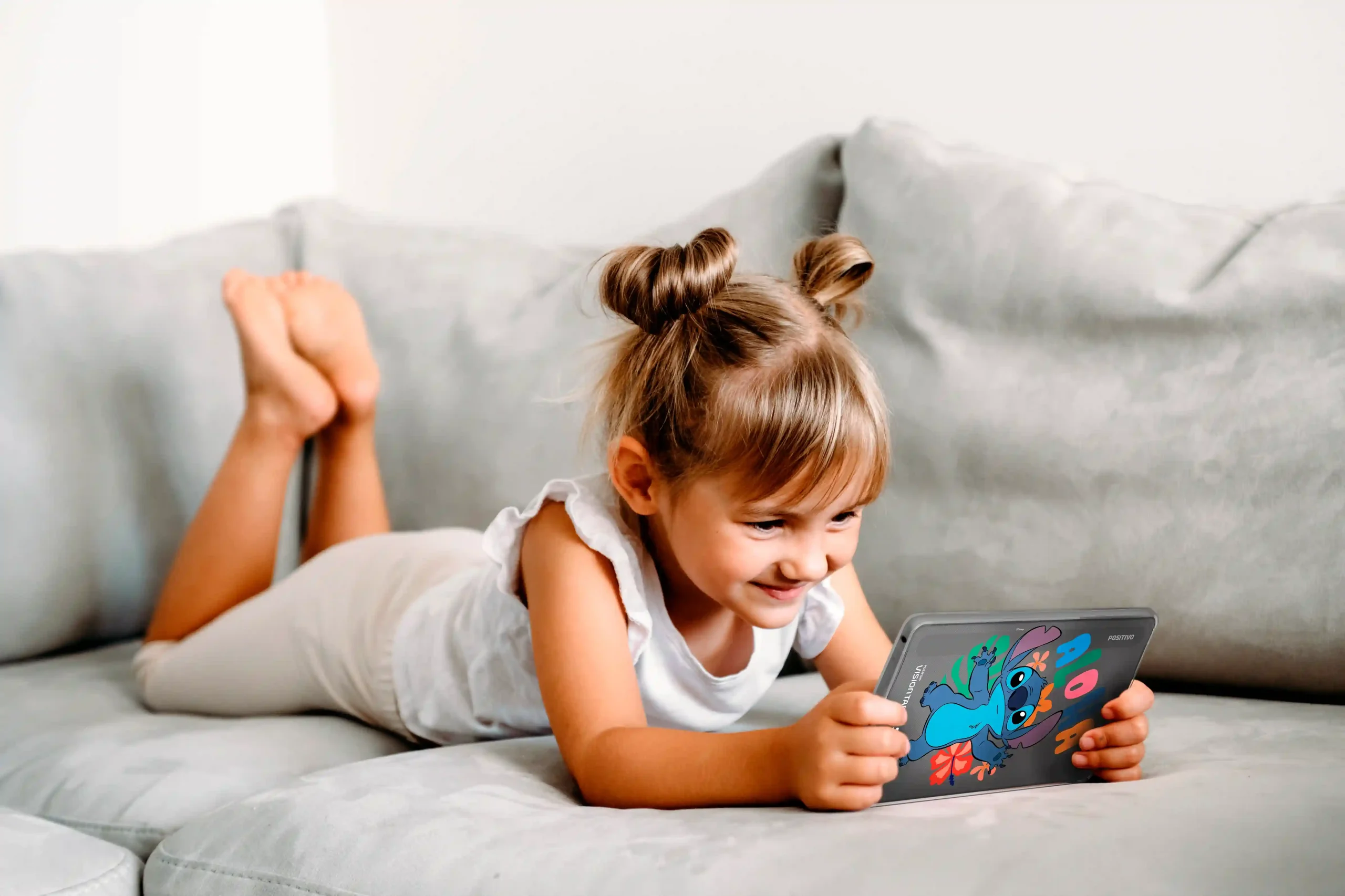 Menina usando Tablet Positivo Vision TAB 7 Stitch com capa personalizada do Stitch, deitada no sofá.